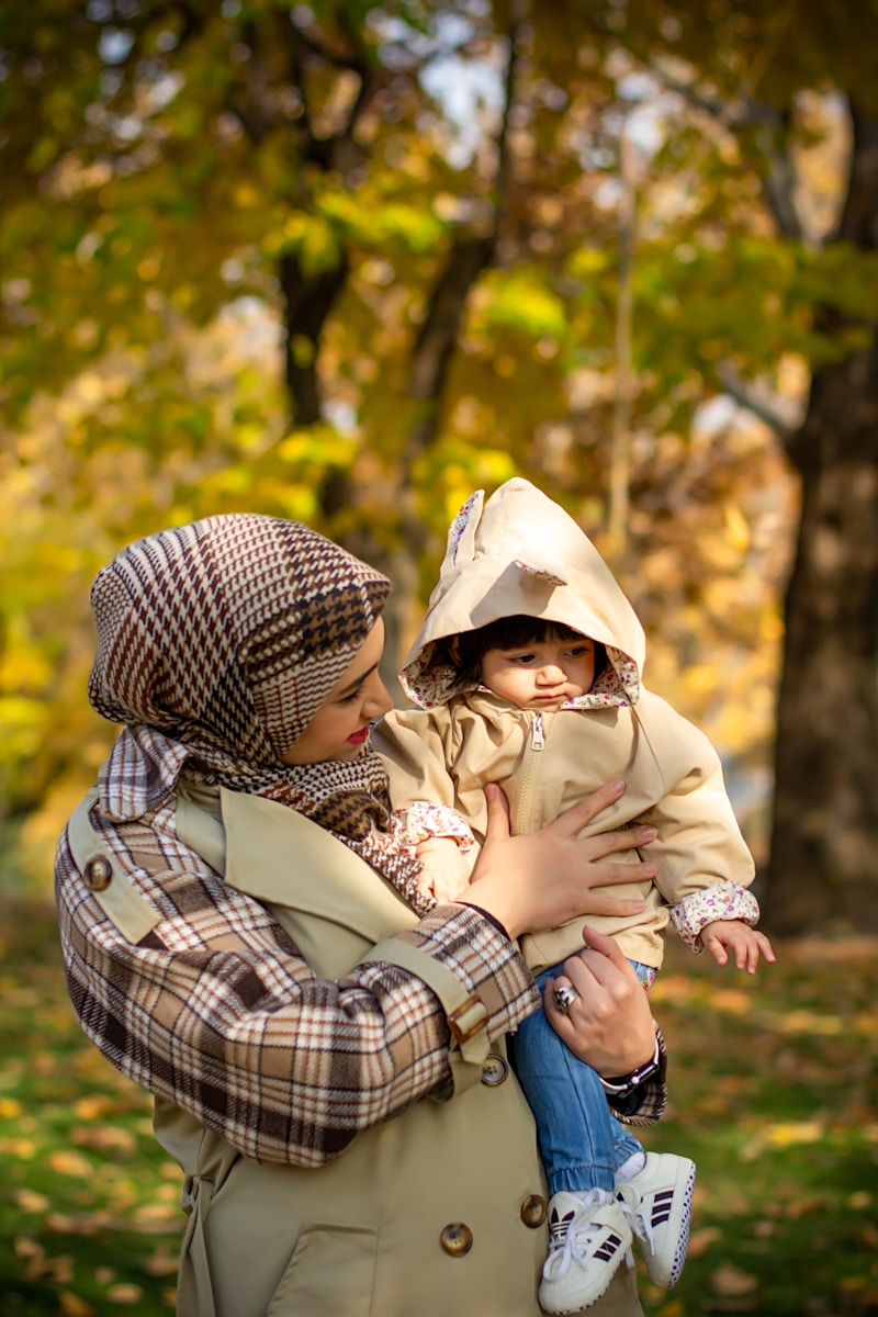 A mother holds her child outdoors in autumn.
